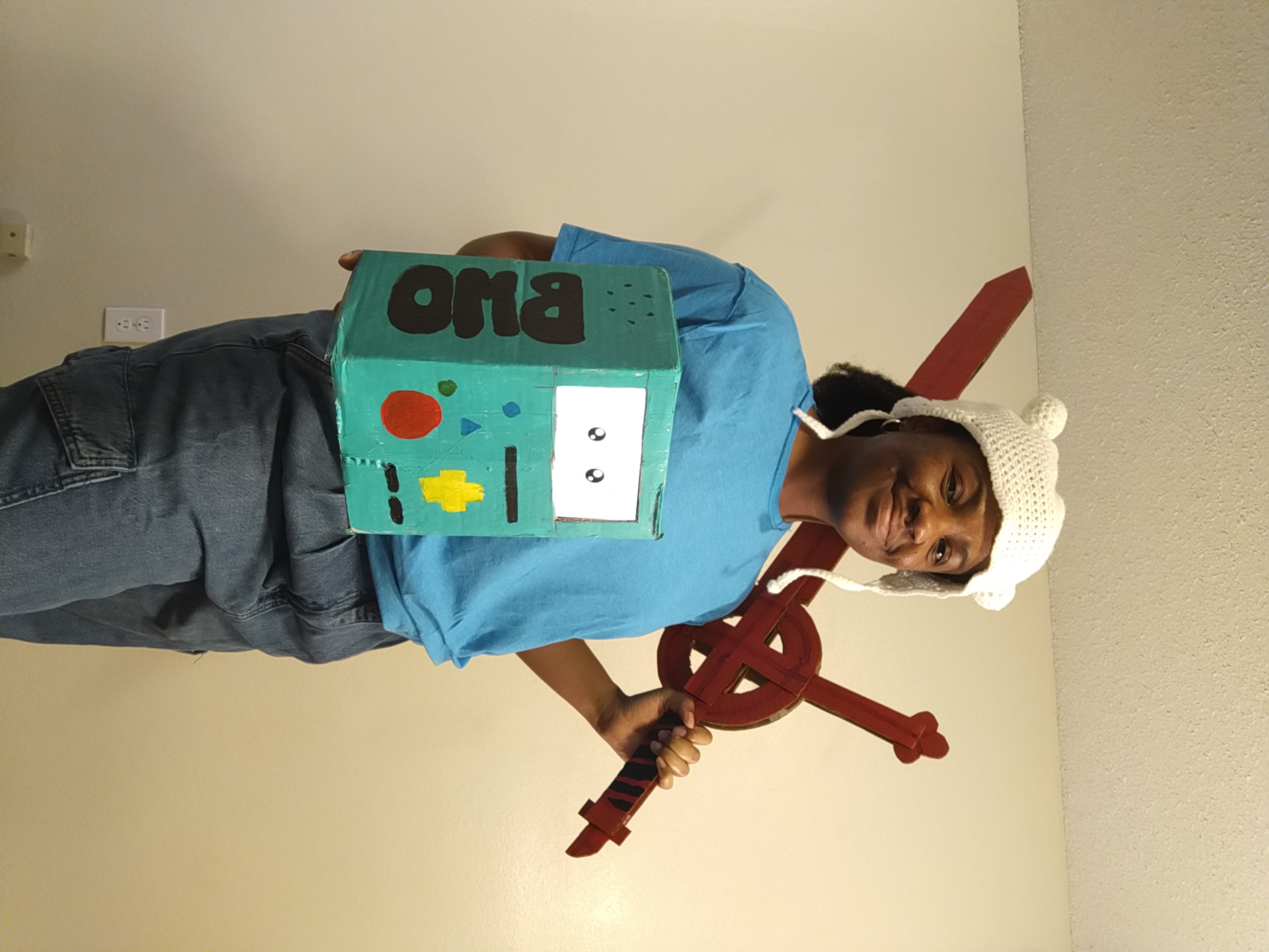 Nyomi Morris posing as Finn while holding up BMO made from painted cardboard with a Peerbots face.